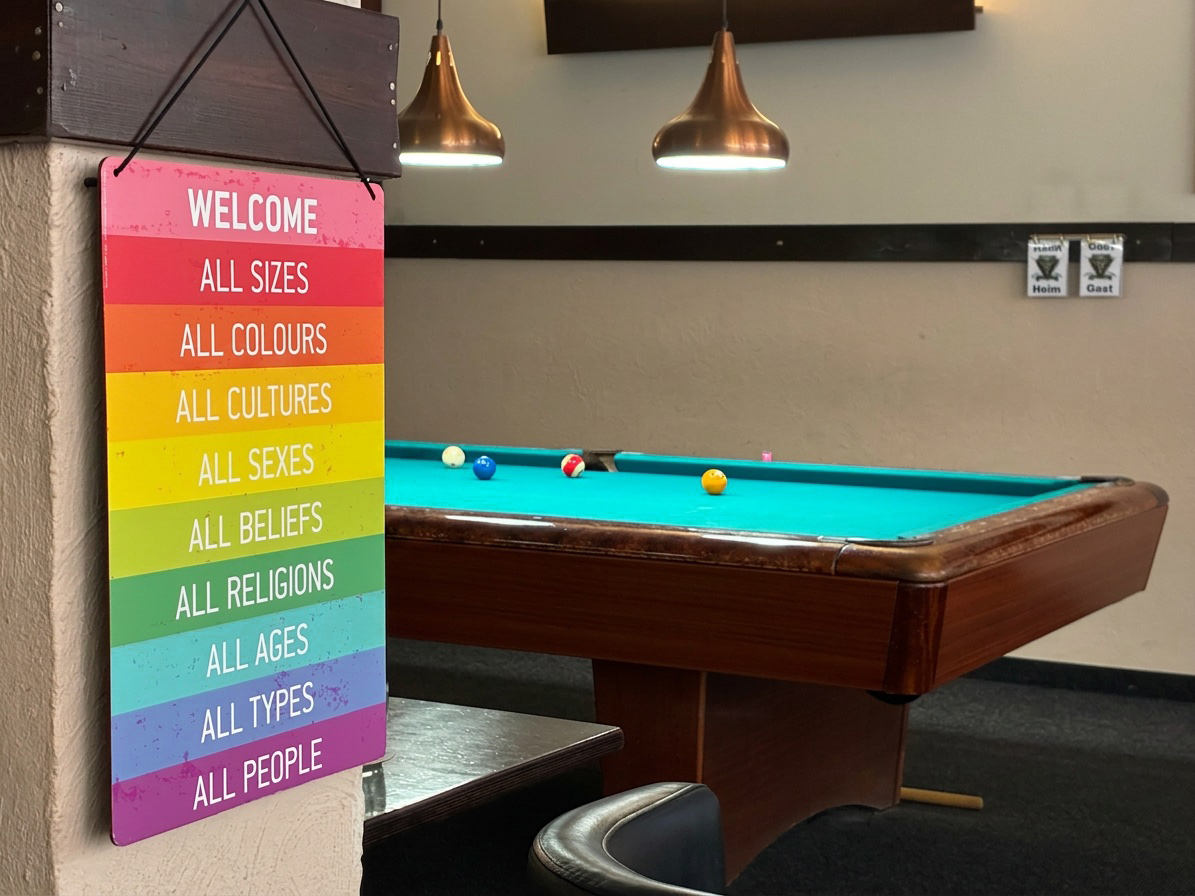 Rainbow-coloured welcome sign next to a pool table